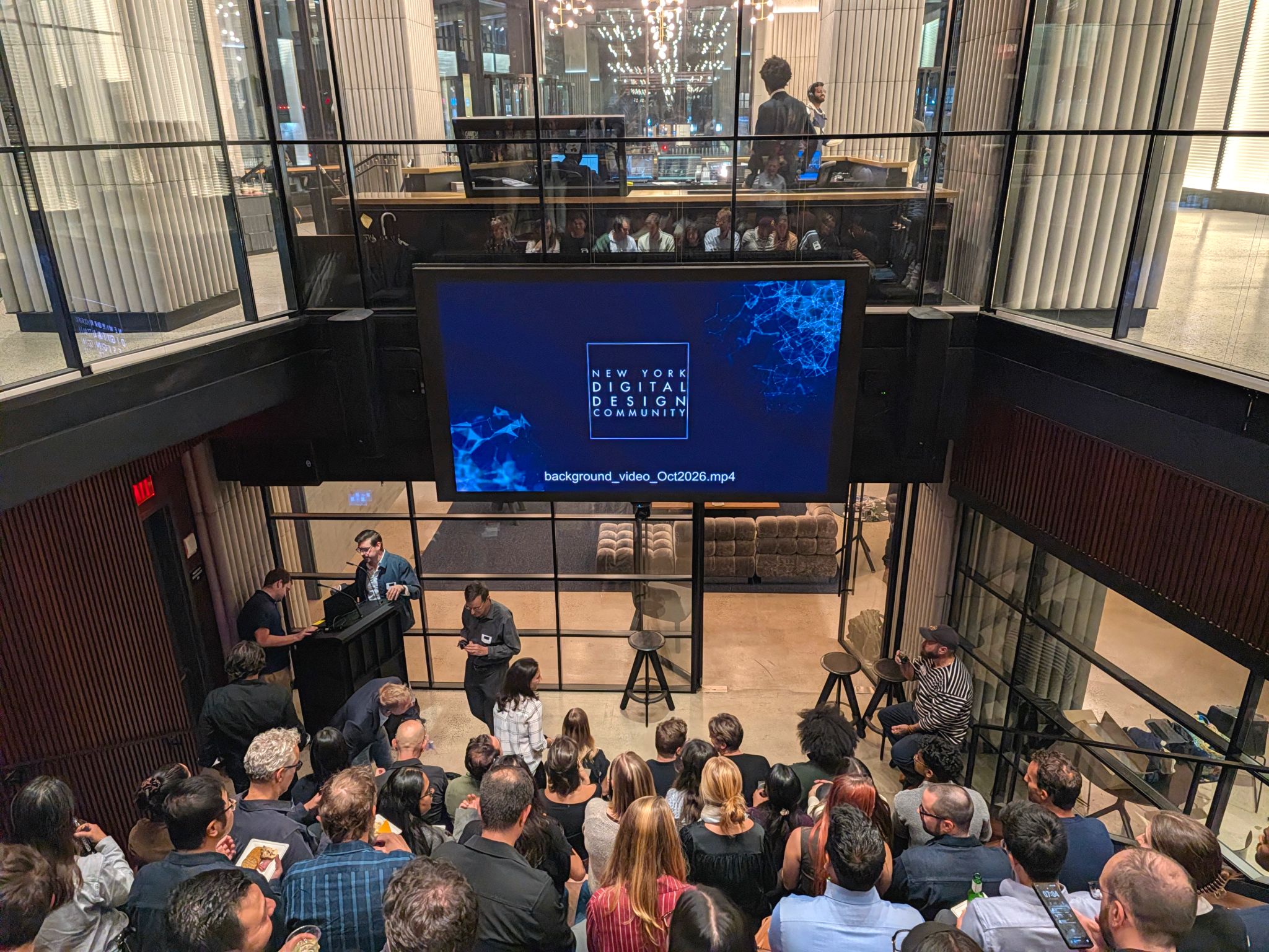 An audience gathered in a two-story event space beneath a screen displaying New York Digital Design Community.