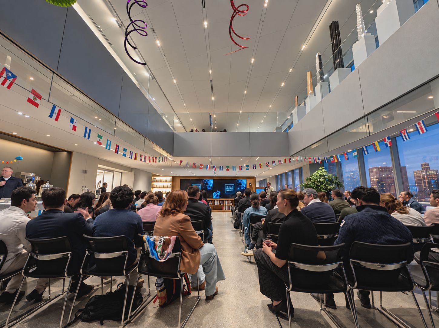 An audience attending a presentation in a bright, two-story event space overlooking the city.